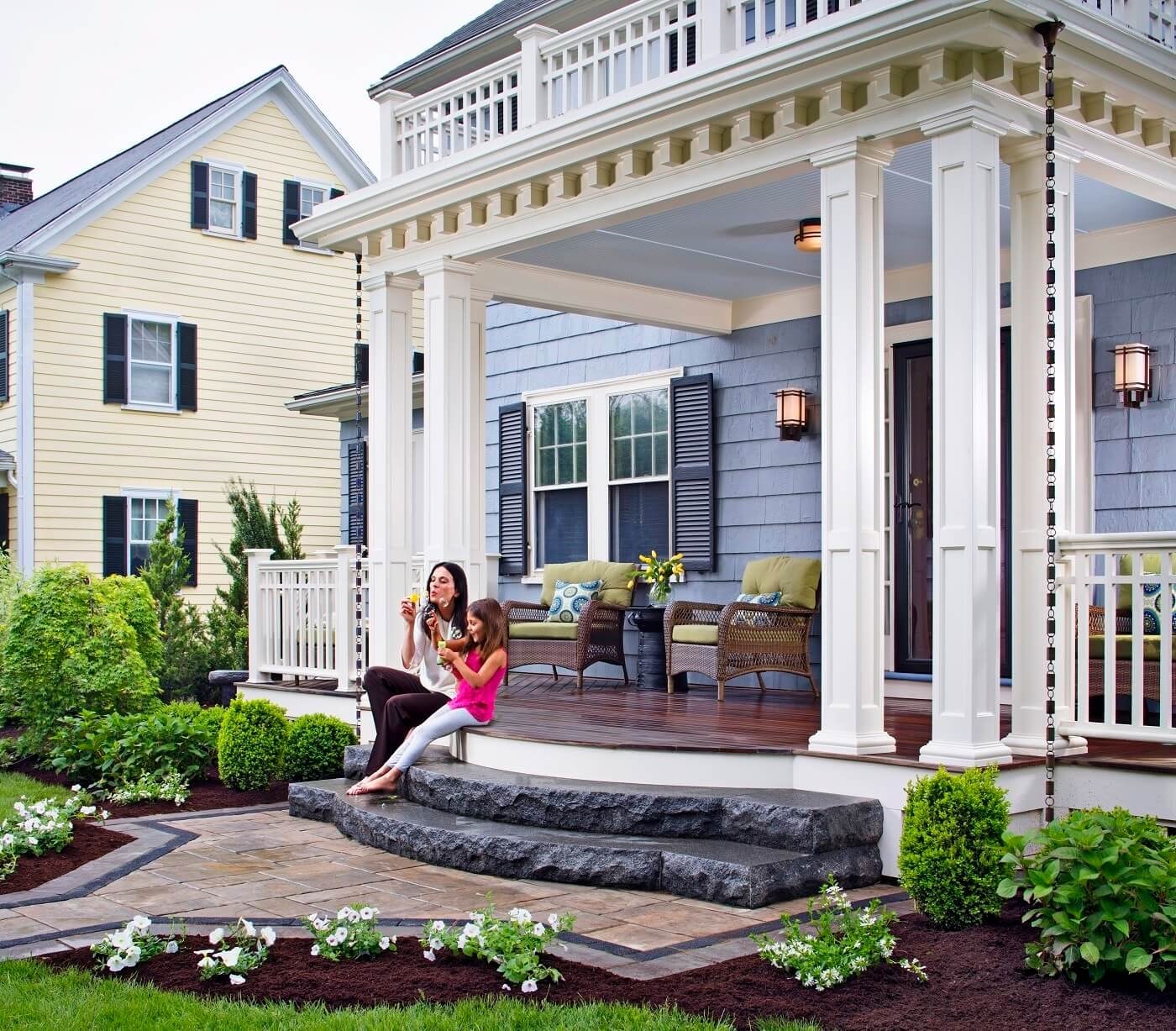 A couple standing together on the front porch of their home, surrounded by tropical plants and natural light