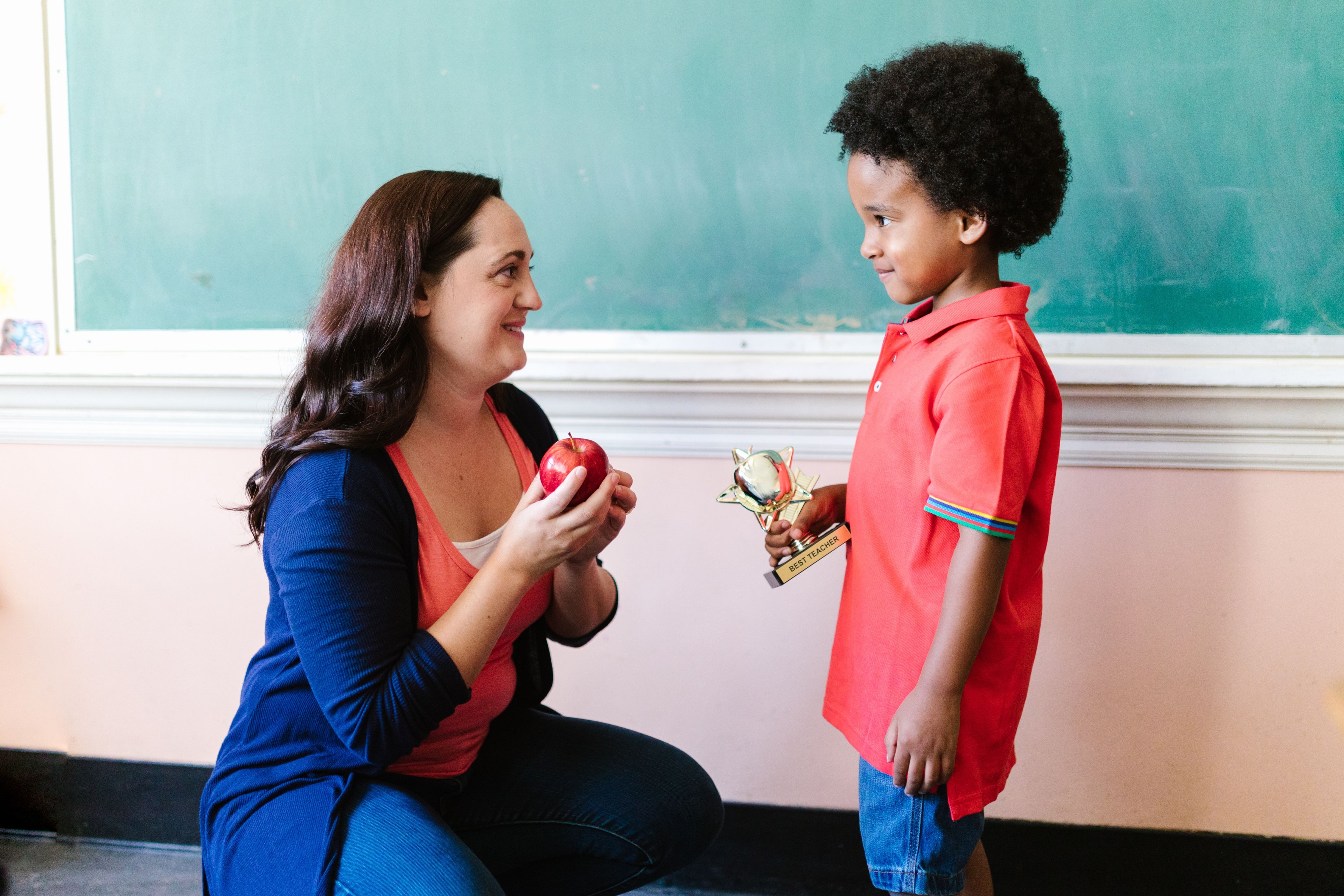 Teacher kneeling to celebrate a young student holding a trophy — education and mentorship
