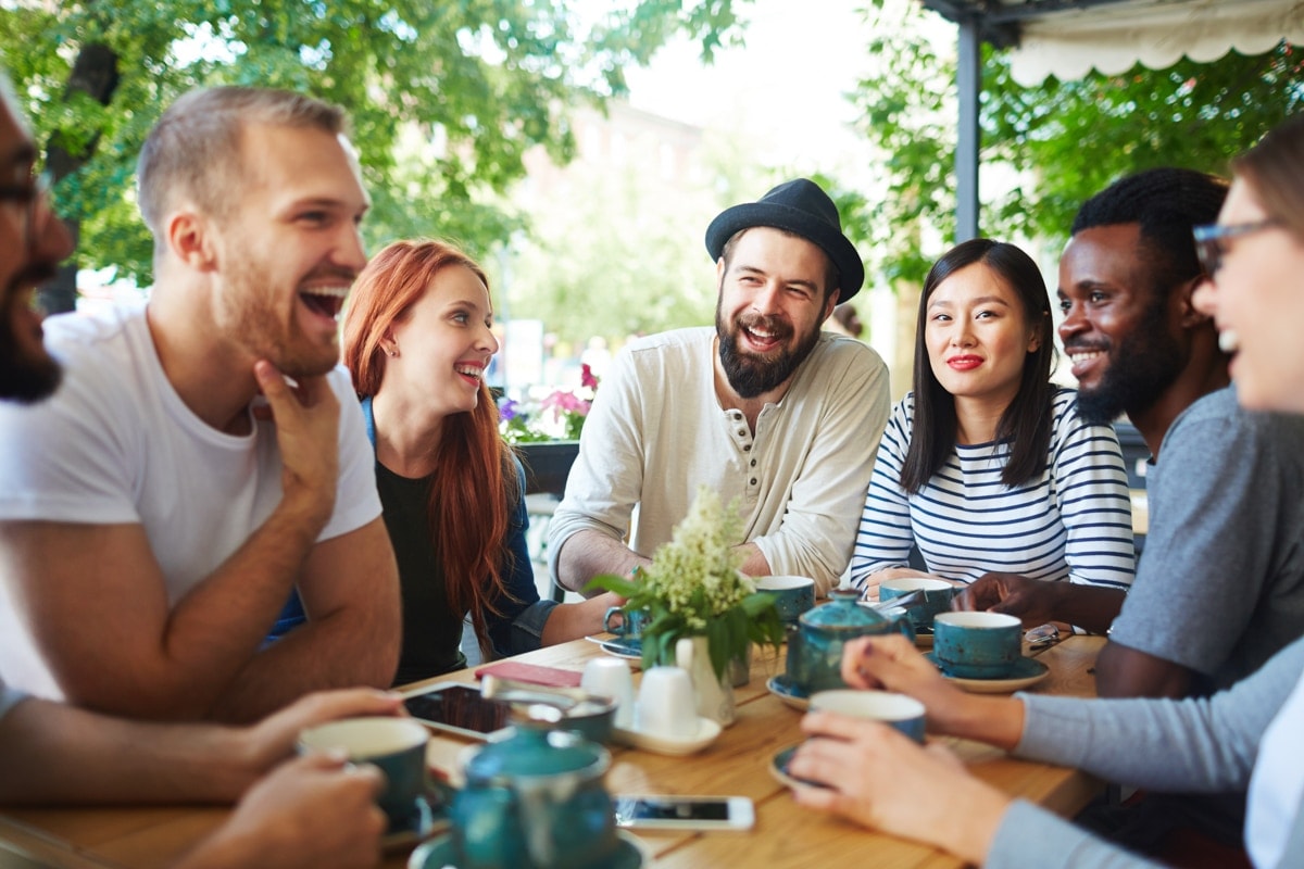 A diverse group of friends laughing together over coffee outdoors — the spirit of Porchaven™ community